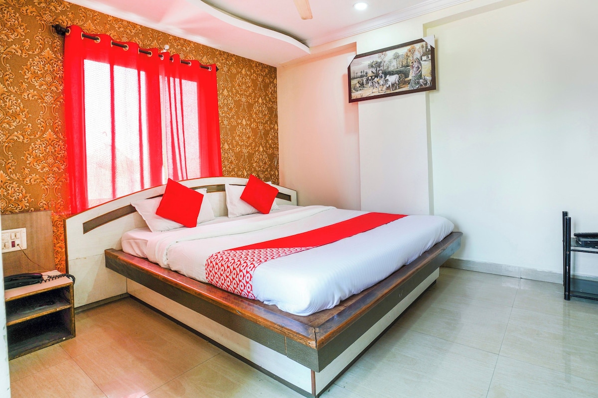 A single-bed room with a wooden frame, white bedding, red accents, a patterned wall, and a painting.