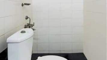 A small, compact bathroom with a white toilet, a shower area, and a window with blinds.