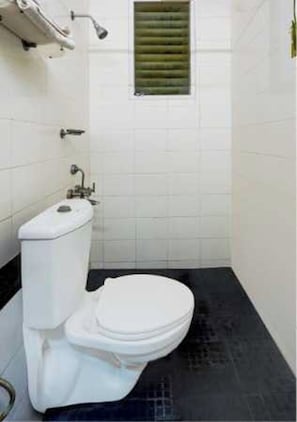 Et lille, kompakt badeværelse med toilet, bruseniche og et vindue med skodder.