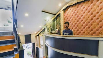 Zona de recepción de un hotel con mostrador curvo, escalera con peldaños naranja y pared decorativa con diseño acolchado.