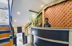 Zona de recepción de un hotel con mostrador curvo, escalera con peldaños naranja y pared decorativa con diseño acolchado.