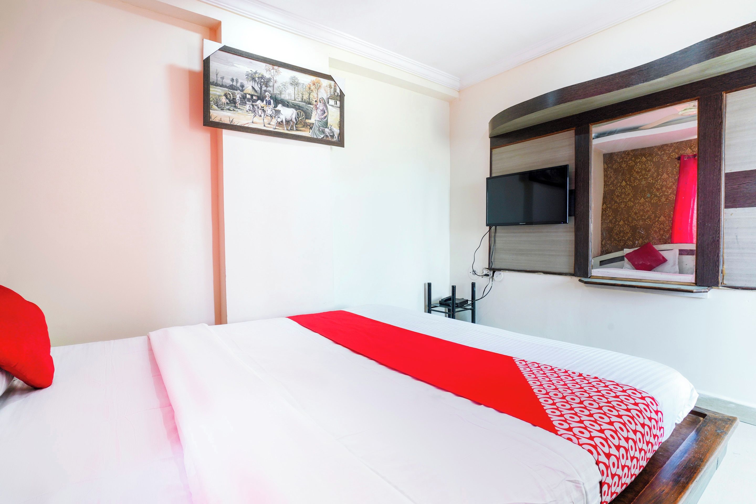 A hotel room with a bed, a television mounted on the wall, and a window with a view of the outside.