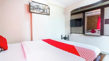 A hotel room with a bed, a television mounted on the wall, and a window with a view of the outside.
