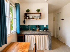 A compact kitchen with a wooden table, a counter with a sink, and a window with curtains. - Hiraya Apartments (San Vicente)