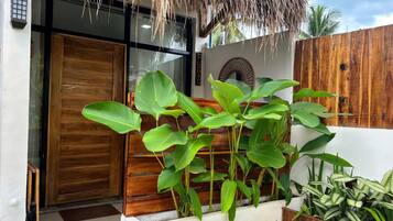 A modern building entrance with a wooden door, a thatched roof, and lush green plants.