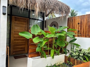A modern building entrance with a wooden door, a thatched roof, and lush green plants.
