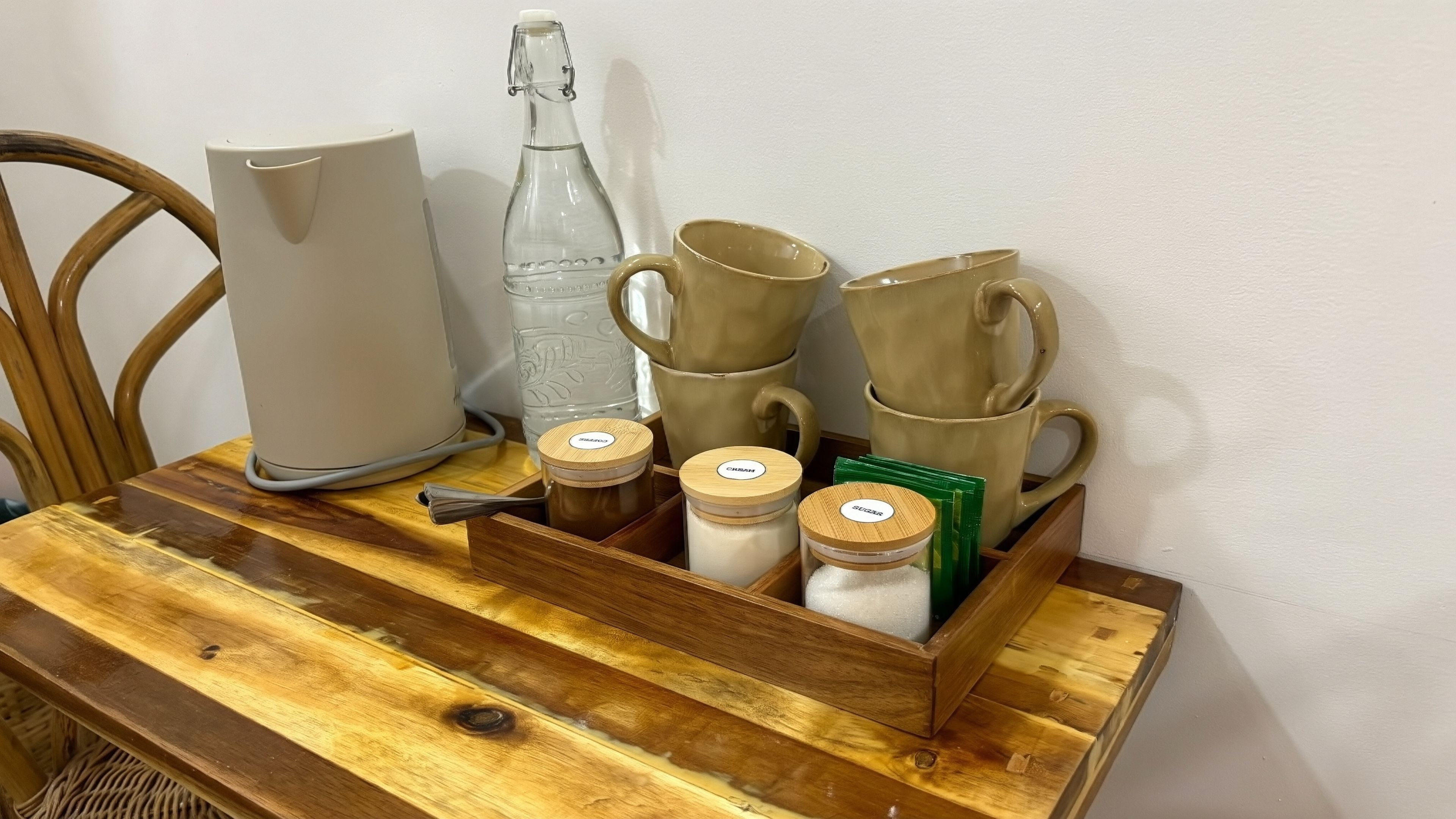 A wooden tray with various kitchen items including a pitcher, a bottle, and jars.