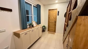 A hallway with a wooden door, a window with blue curtains, a cabinet with a picture frame, and a potted plant.