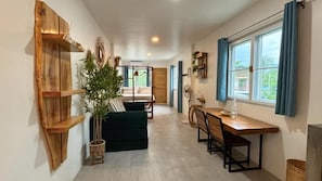 A room with a wooden shelf, a green sofa, a dining table with chairs, and a window with curtains. - Hiraya Apartments (San Vicente)