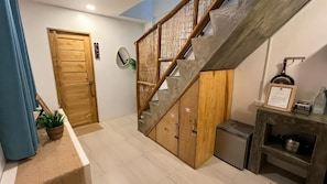 A staircase with a wooden handrail and a metal banister, leading to a room with a door and a small cabinet. - Hiraya Apartments (San Vicente)