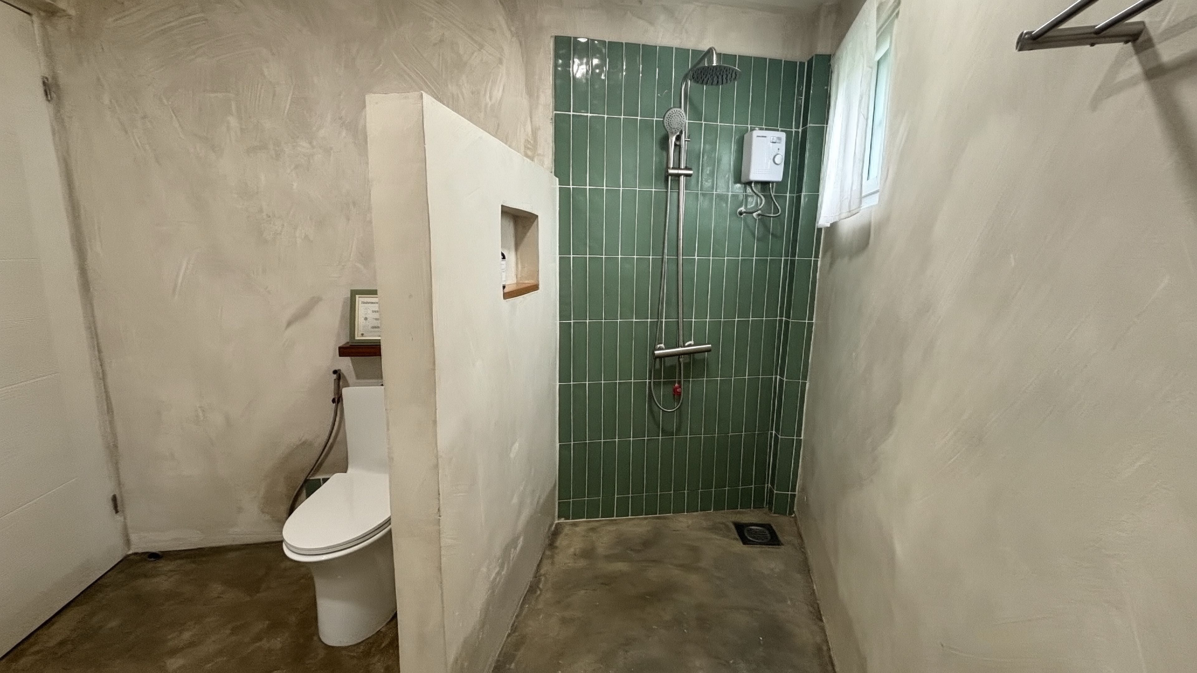 Een kleine, smalle badkamer met toilet, een douchegedeelte met een groene betegelde muur en een wit wastafelmeubel.