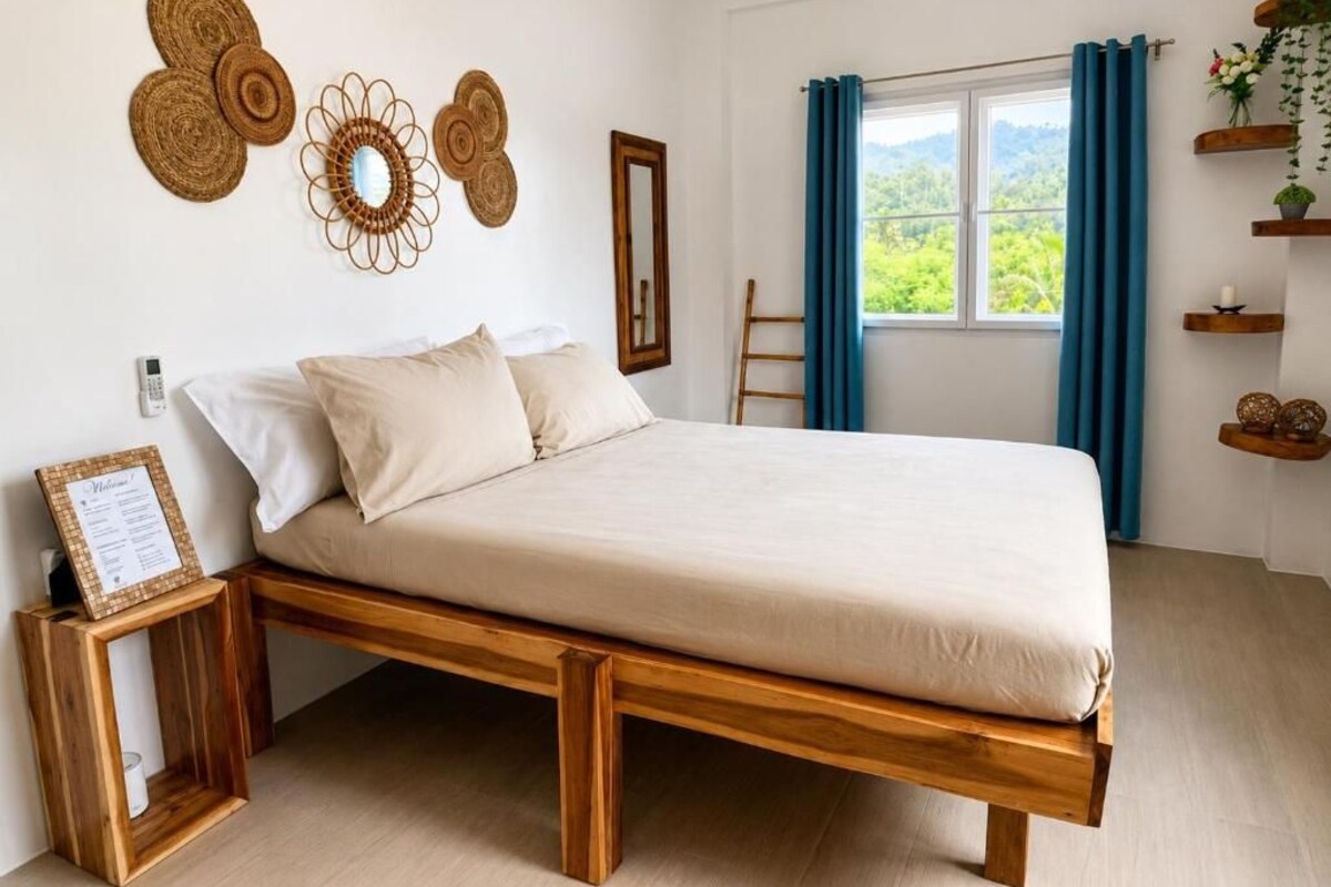 Una habitación con una cama de madera, una mesita de noche pequeña, un espejo en la pared y una ventana con cortinas.