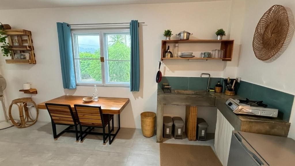 Una cocina compacta con mesa, sillas, una ventana con cortinas y estantes empotrados con utensilios de cocina.