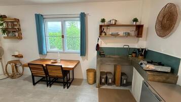 Una cocina compacta con mesa, sillas, una ventana con cortinas y estantes empotrados con utensilios de cocina.