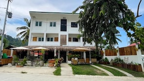 A two-story building with a central entrance, outdoor seating area with umbrellas, and a well-maintained garden. - Hiraya Apartments (San Vicente)
