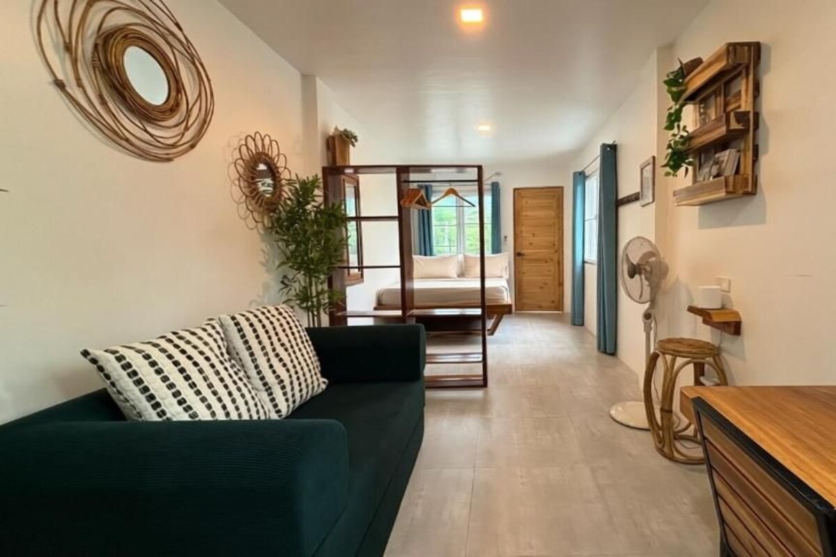 Una habitación con un sofá, una mesa de madera, un ventilador y una cama al fondo.