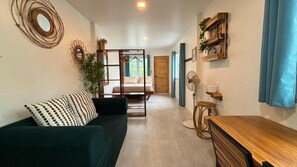 A room with a sofa, a wooden table, a fan, and a bed in the background. - Hiraya Apartments (San Vicente)