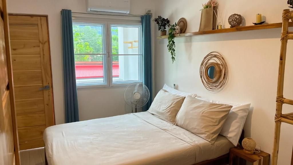 Ein Zimmer mit einem Bett, einem Vorhangfenster, einem Ventilator und einem Regal mit Dekoration.