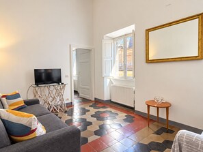 A living room with a sofa, a television, a small table, and a window with a view. - Appartamento Chiavari by Geco Vacation Rentals (Rome)