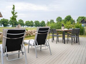 An outdoor deck with metal-framed chairs and a table, overlooking a body of water and greenery. - House 11 - Meadow Pipit (Am Salzhaff)
