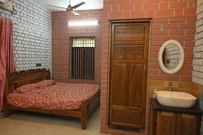 A bedroom with a bed, a wooden door, a window with bars, a mirror, and a bathroom with a sink.