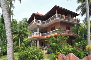 A multi-story building with balconies, surrounded by lush greenery and palm trees.