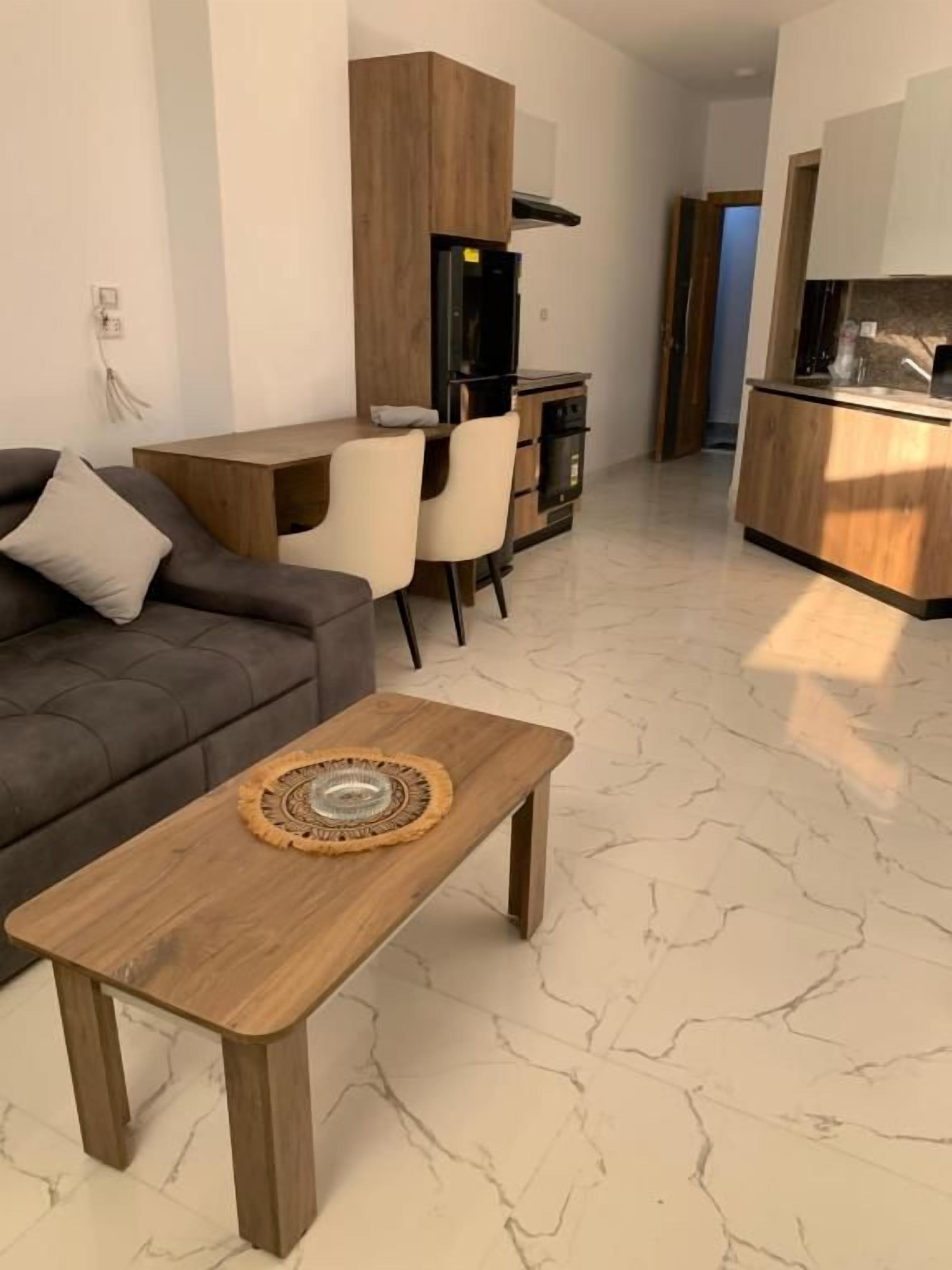 Een moderne woonkamer met een bank, een houten salontafel en een keuken in de achtergrond.