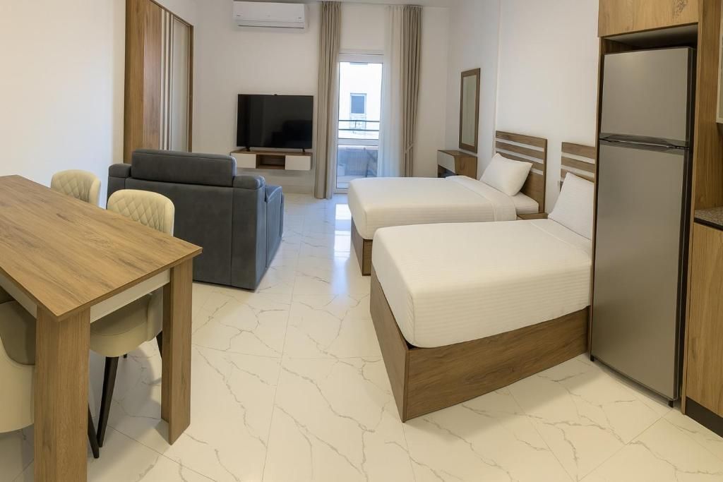 Een hotelkamer met een houten bureau, twee bedden, een bank, een televisie en een koelkast.