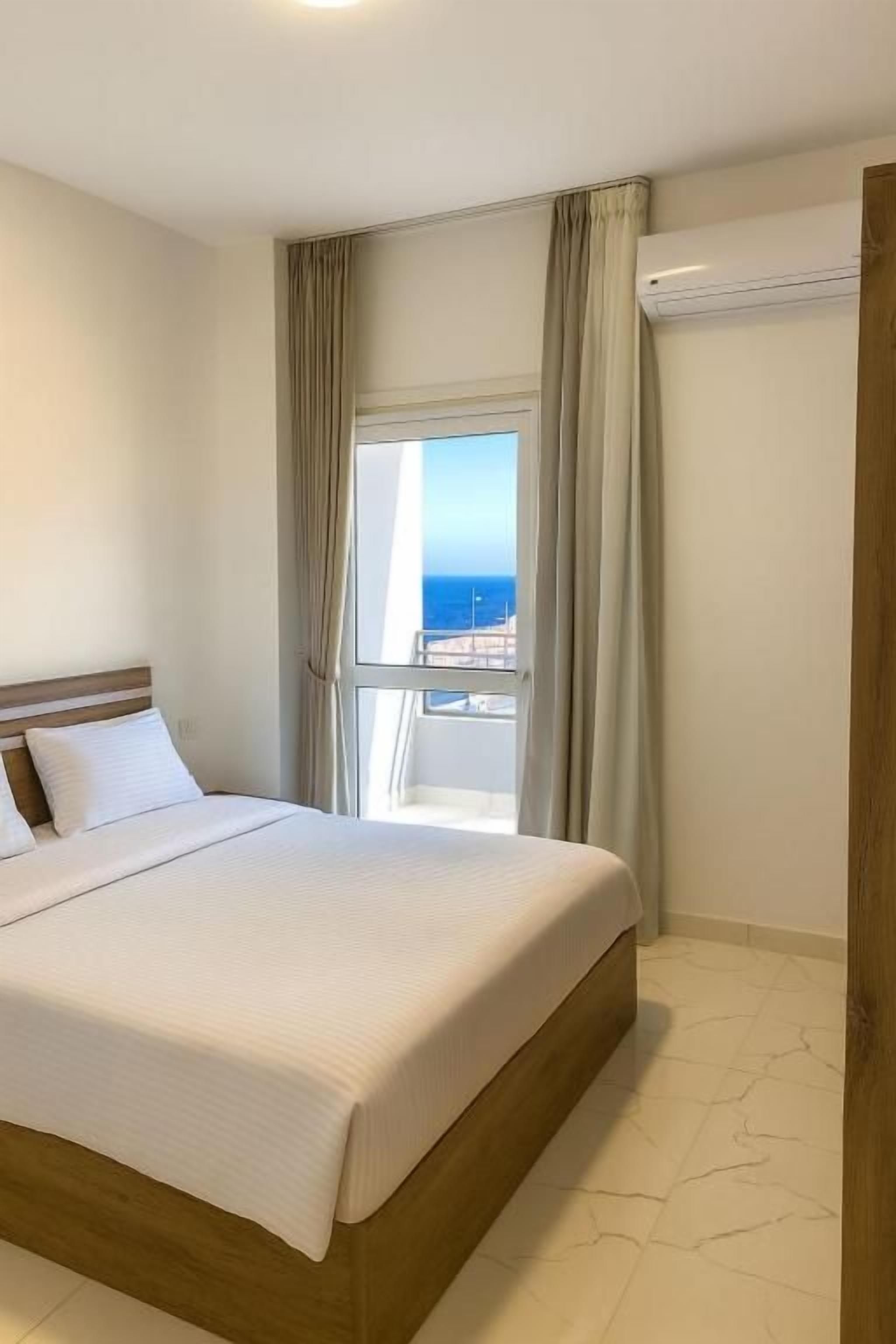 A hotel room with a large bed, a window with curtains, and a view of the sea.