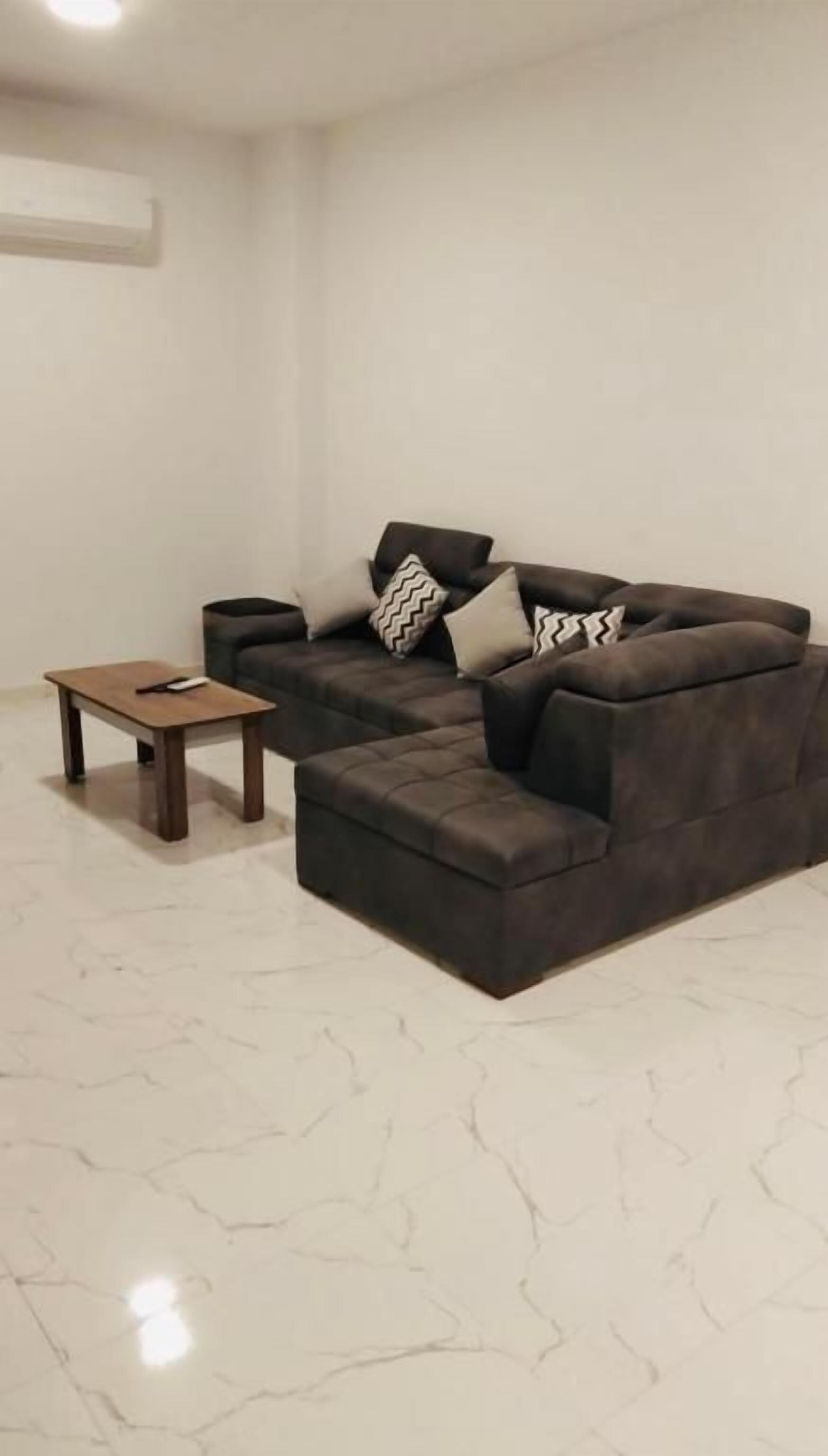 Una sala de estar con un sofá modular, una mesita de madera y un piso de mármol blanco.