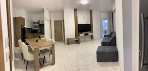A modern living space with a dining area, a sofa, and a TV mounted on the wall. - Hurghada Concierge La Prestigia (Red Sea Governorate)