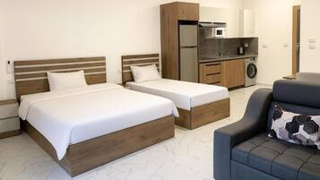 Ein Hotelzimmer mit zwei Betten, einer Couch, einer Waschmaschine und einer Küchenzeile.