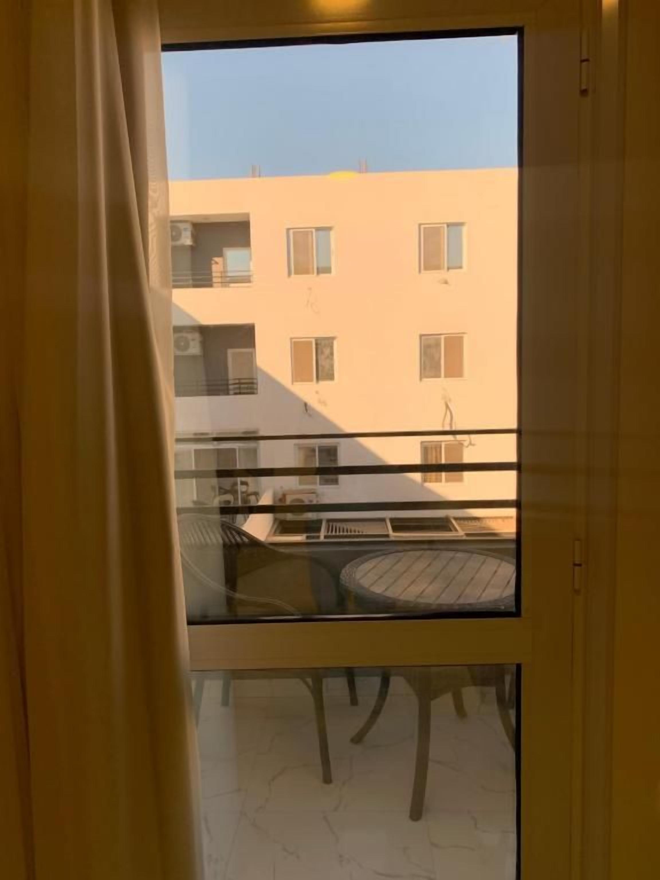 Ein Balkon mit Glastür, einem runden Tisch und Blick auf ein Gebäude mit vielen Fenstern.