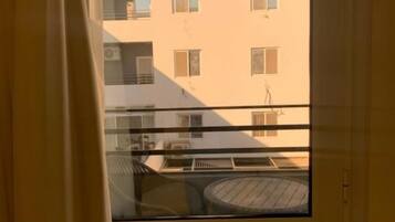 Ein Balkon mit Glastür, einem runden Tisch und Blick auf ein Gebäude mit vielen Fenstern.
