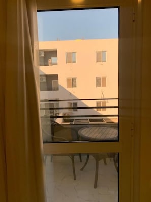 A balcony with a glass door, a round table, and a view of a building with multiple windows. - by Hurghada Concierge mountain (Red Sea Governorate)