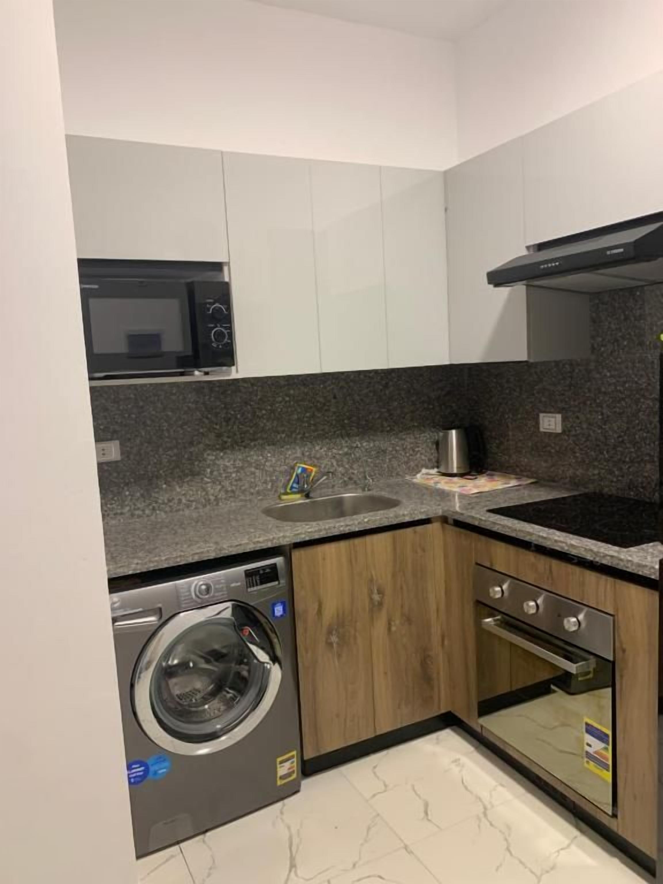 A compact kitchen with a washing machine, oven, microwave, and a sink.