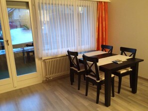 A dining area with a table and chairs, a window with curtains, and a radiator. - Quellenhof A07 Appartement/Fewo, Dusche oder Bad, WC 1½-Zimmerwohnung by Interhome (Davos)