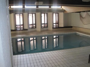 Piscina com pavimento em azulejos e amplas janelas.