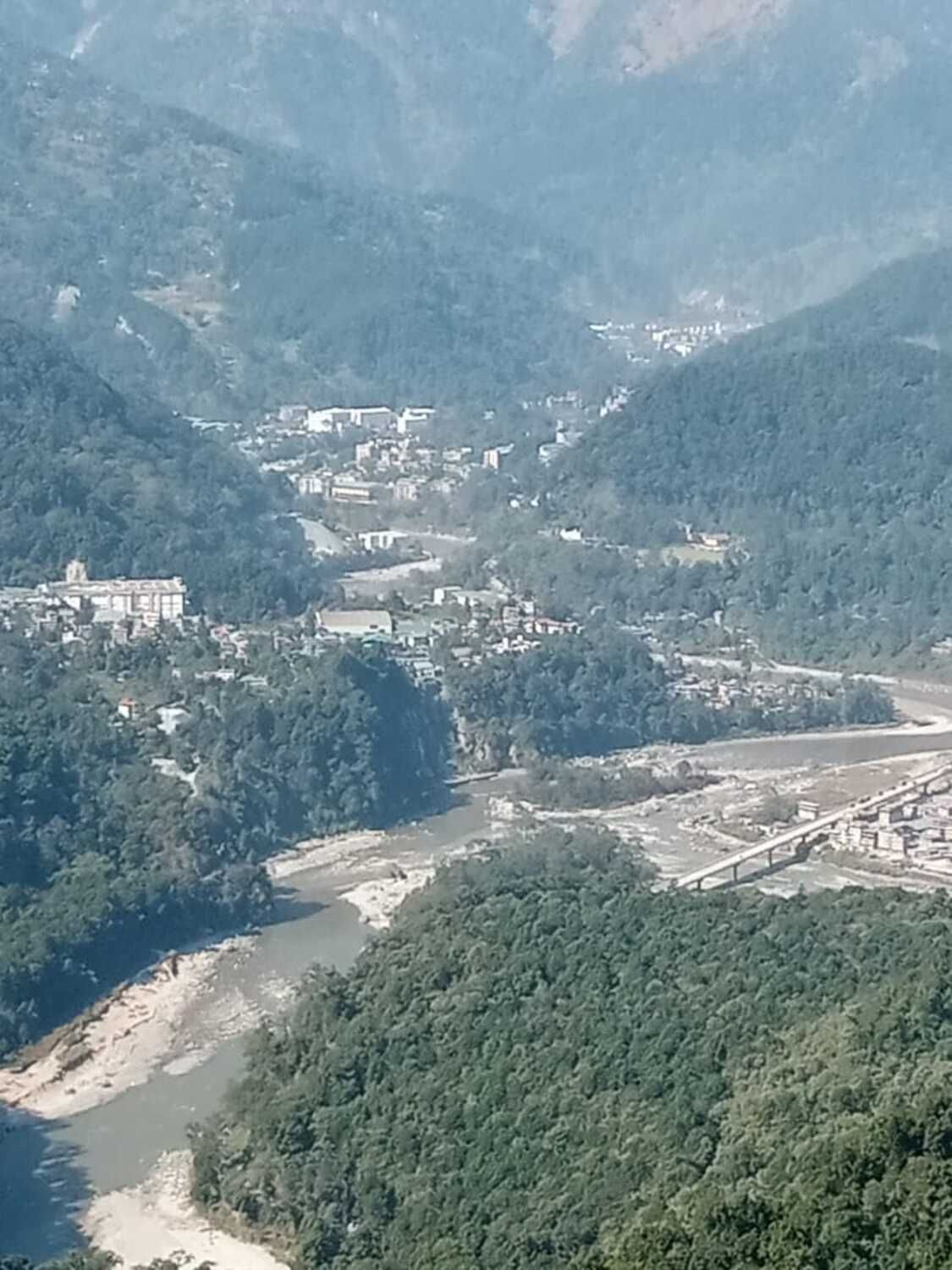 Een bergachtig landschap met een rivier, een brug en verspreide gebouwen.