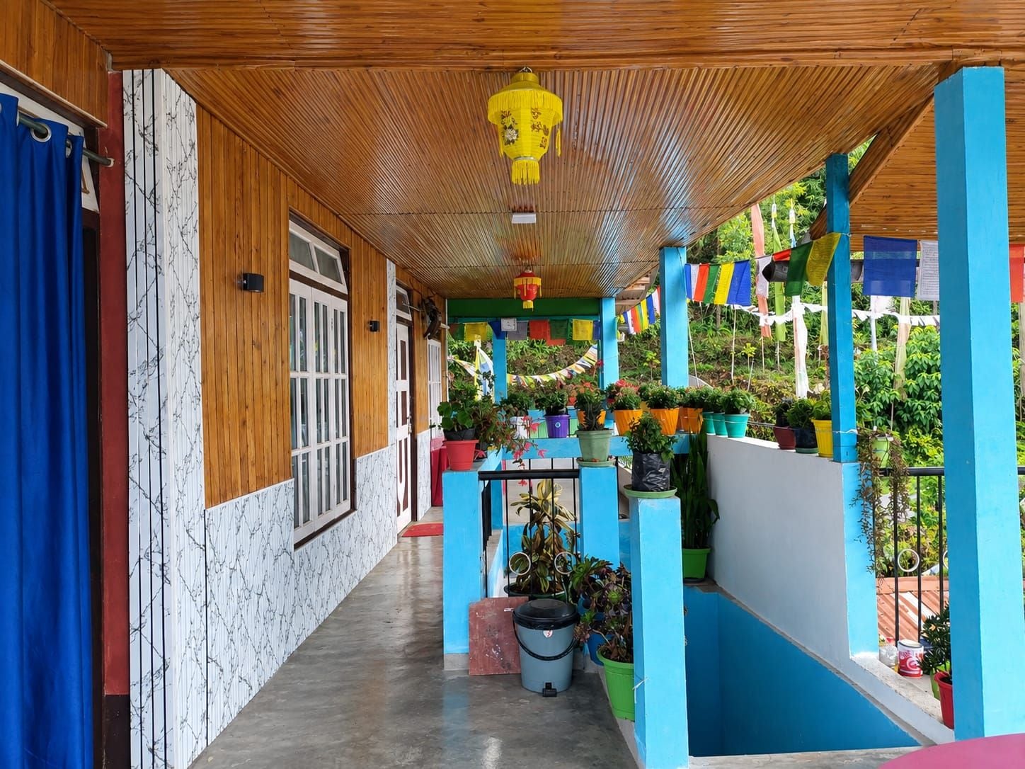 A covered outdoor corridor with wooden ceiling, colorful flags, and potted plants.