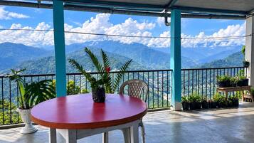 A covered outdoor seating area with a table and chairs, overlooking a mountainous landscape.
