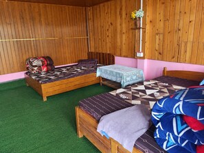 A room with two wooden beds, a small table, and a wall-mounted shelf with flowers. - Satyam Homestay (Kalimpong)