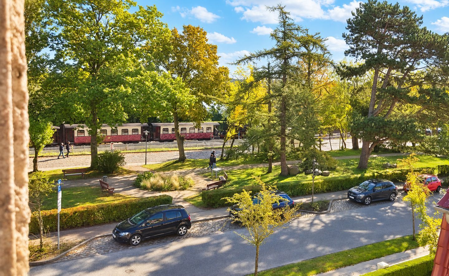 Eine Wohnstraße mit parkenden Autos, einem Fußweg und einem Zug im Hintergrund.