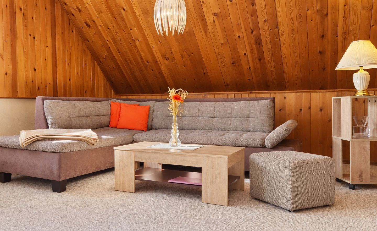Ein gemütliches Zimmer mit Holzbalkendecke, einem grauen Sofa, einem Holztisch und einem kleinen Hocker.
