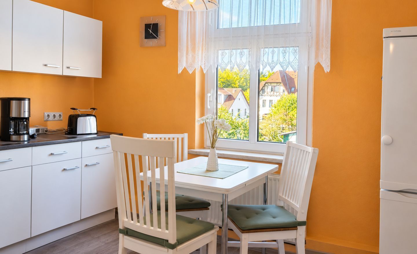 Een keuken met witte kasten, een koffiezetapparaat en een raam met uitzicht op huizen.