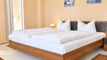 A double bed with a wooden frame, white bedding, and a nightstand with a lamp.
