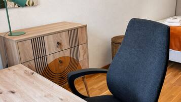 A room with a wooden table, a blue chair, a cabinet with a geometric design, and a wall-mounted lamp.
