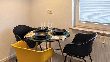 A dining area with a table set for two, a black pendant light, and a window with blinds.