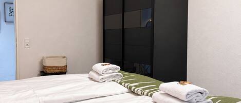 Camera d'albergo con due letti, un armadio, un tavolino con un cesto e un quadro appeso al muro.