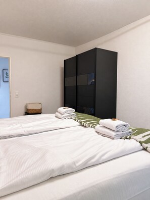 A hotel room with two beds, a wardrobe, a small table with a basket, and a framed picture on the wall. - 7 Seas City-Apartment 68  (Saarbrücken)